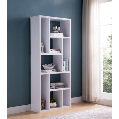 The Versatile Display Cabinet, a modern white piece with asymmetrical shelves, holds books, decor, and a plant. It stands against a teal wall by a window with sheer curtains on a light wood floor.