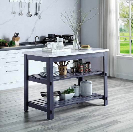A modern kitchen showcases the Enapay - Marble Top Kitchen Island in Gray, featuring a white marble top and dark shelves with glassware, jars, dishes, and a potted plant. Sunlight from a large window enhances the sleek, clean decor.