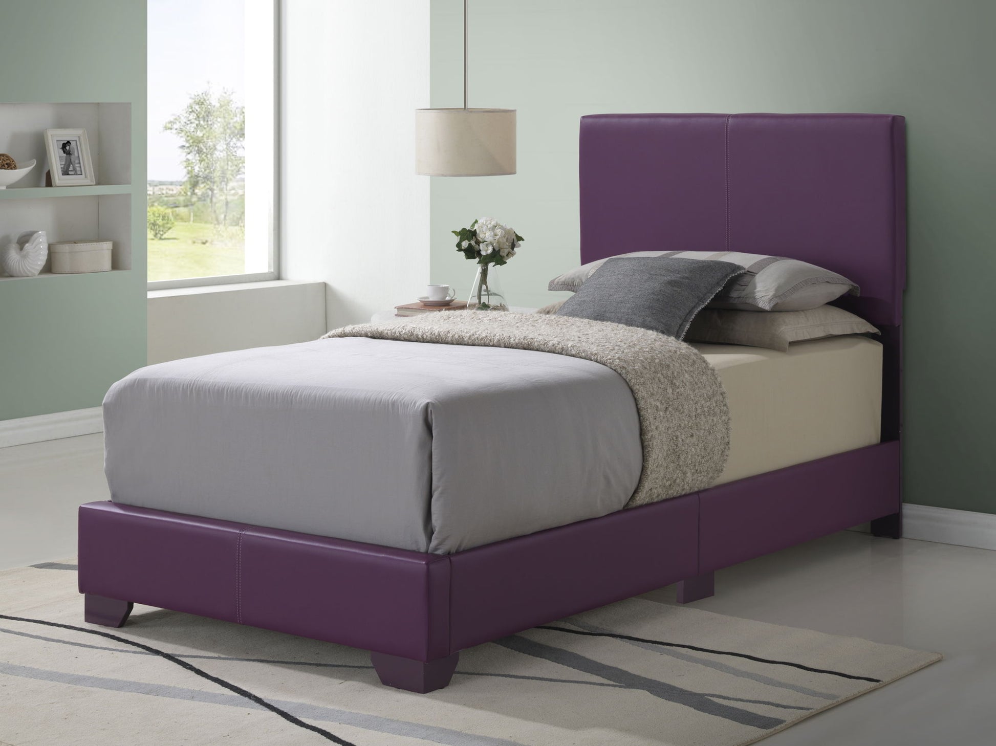 A modern bedroom features the Elegant Platform Bed For Relaxed Spaces in purple upholstery with gray bedding, a beige blanket, and two pillows. A lamp, vase of flowers, decor accents on a side table by the window, and a rug adorn the light floor.