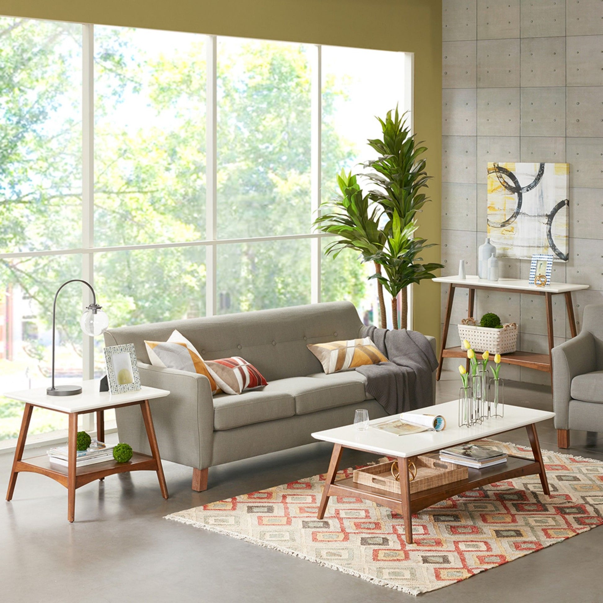 A modern living room with large windows, a gray sofa, white coffee table, Modern Table With Extra Storage, lamp side table, green plants, colorful rug, and abstract art. Natural light fills the inviting space.