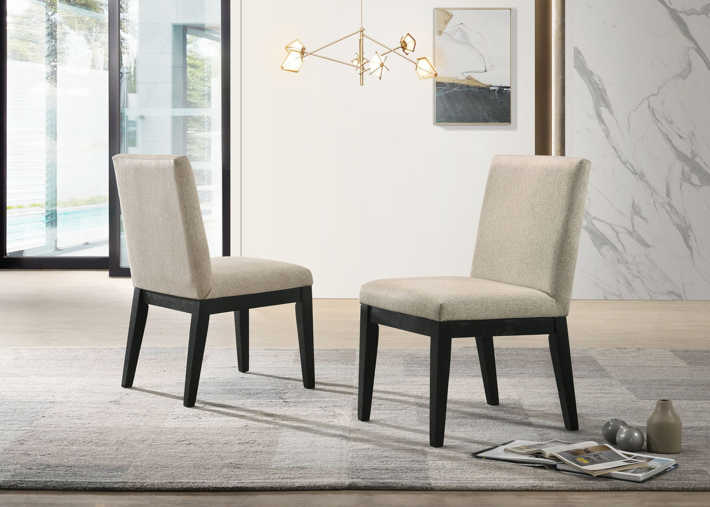 A set of two Jasper Contemporary Fabric 19" Dining Chairs in beige, featuring dark wooden legs, face each other on a gray rug in a modern room with large windows, a contemporary light fixture, and stylish decor.