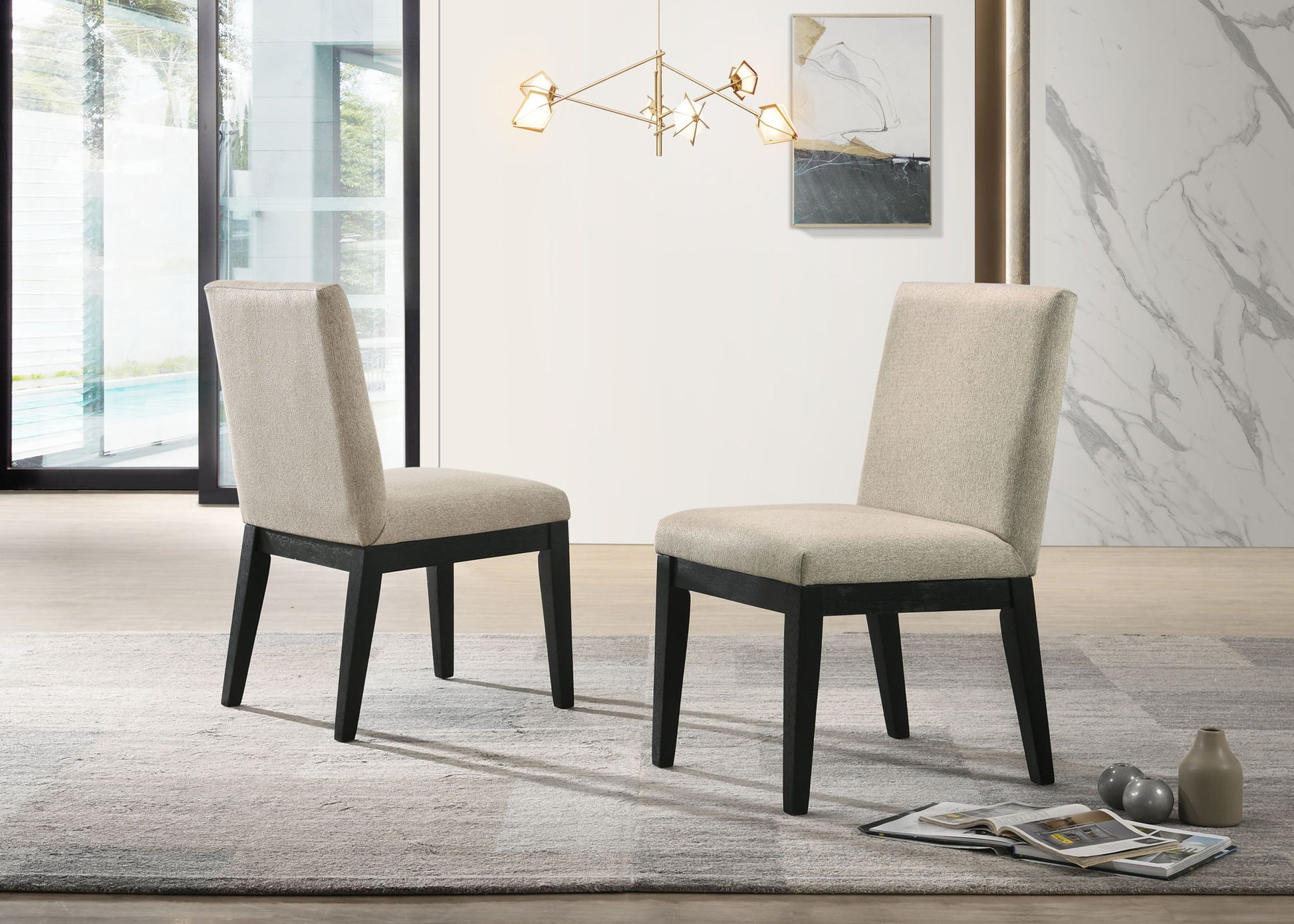 A set of two Jasper Contemporary Fabric 19" Dining Chairs in beige, featuring dark wooden legs, face each other on a gray rug in a modern room with large windows, a contemporary light fixture, and stylish decor.