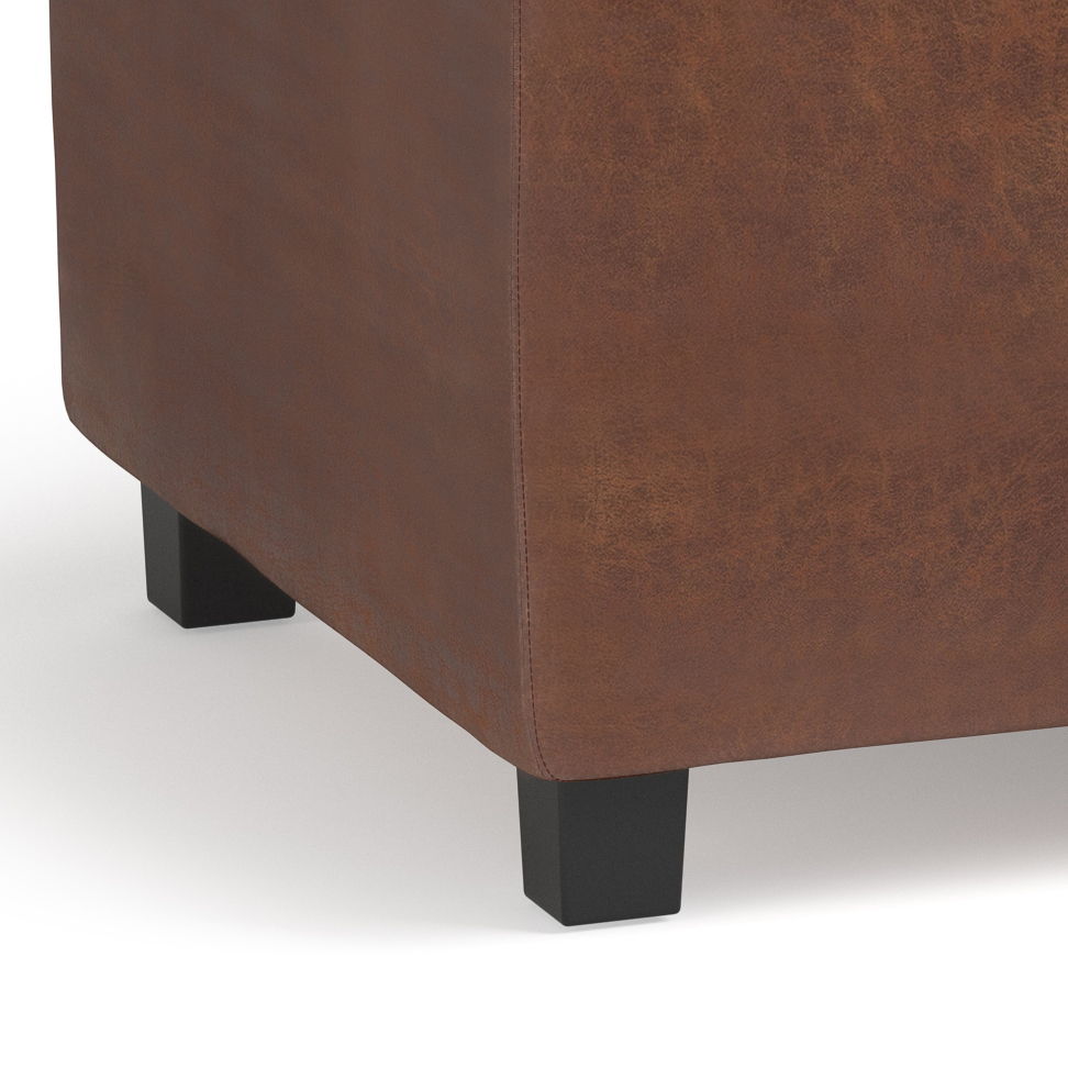 Close-up of the bottom corner of the Avalon Upholstered Storage Ottoman in brown leather with visible stitching, featuring two short black wooden legs on a white background.