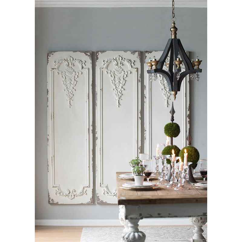 A dining area features a rustic wooden table with candles, glassware, and plants beneath a black chandelier. The gray wall is decorated with a Set Of Large Wooden Rectangle Hanging Panels.