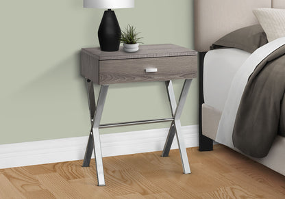 The Accent Side X Table with a storage drawer and contemporary gray wood finish stands by the bed, featuring chrome X legs. On top are a black-and-white lamp and a small green potted plant.