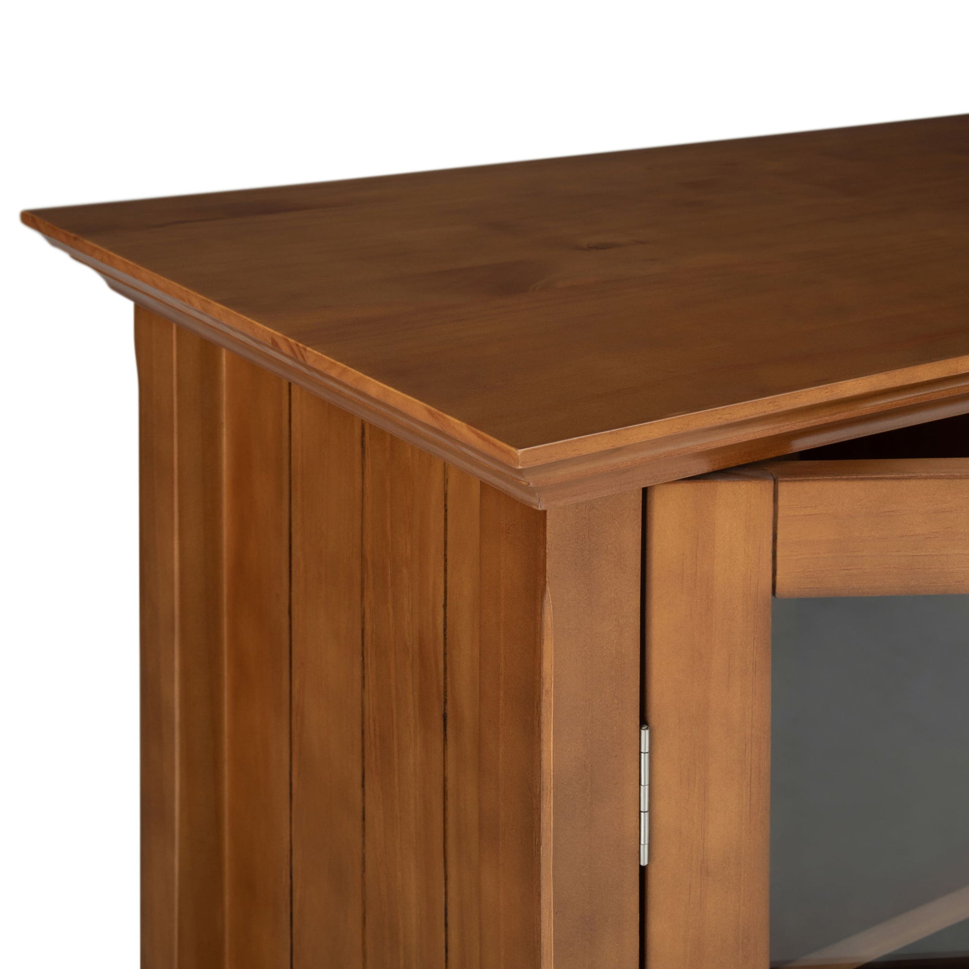Close-up of the top corner of the Acadian - Medium Storage Cabinet, Handcrafted, featuring the smooth wood grain, side panel, glass door, and detailed door hinge.