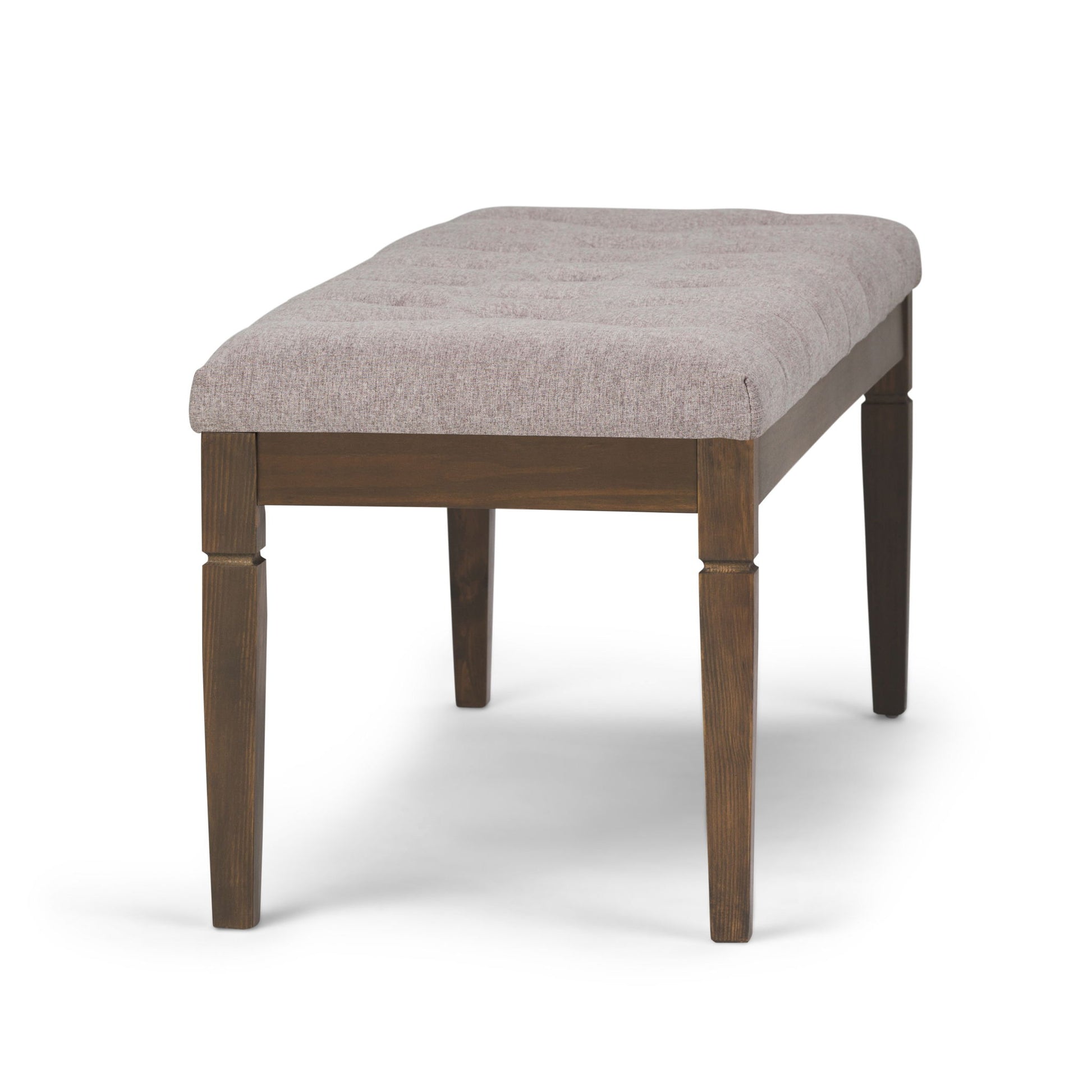 The Waverly Upholstered Tufted Ottoman Bench features a four-leg wooden base and a padded light gray fabric seat with a simple, modern design, shown against a white background.