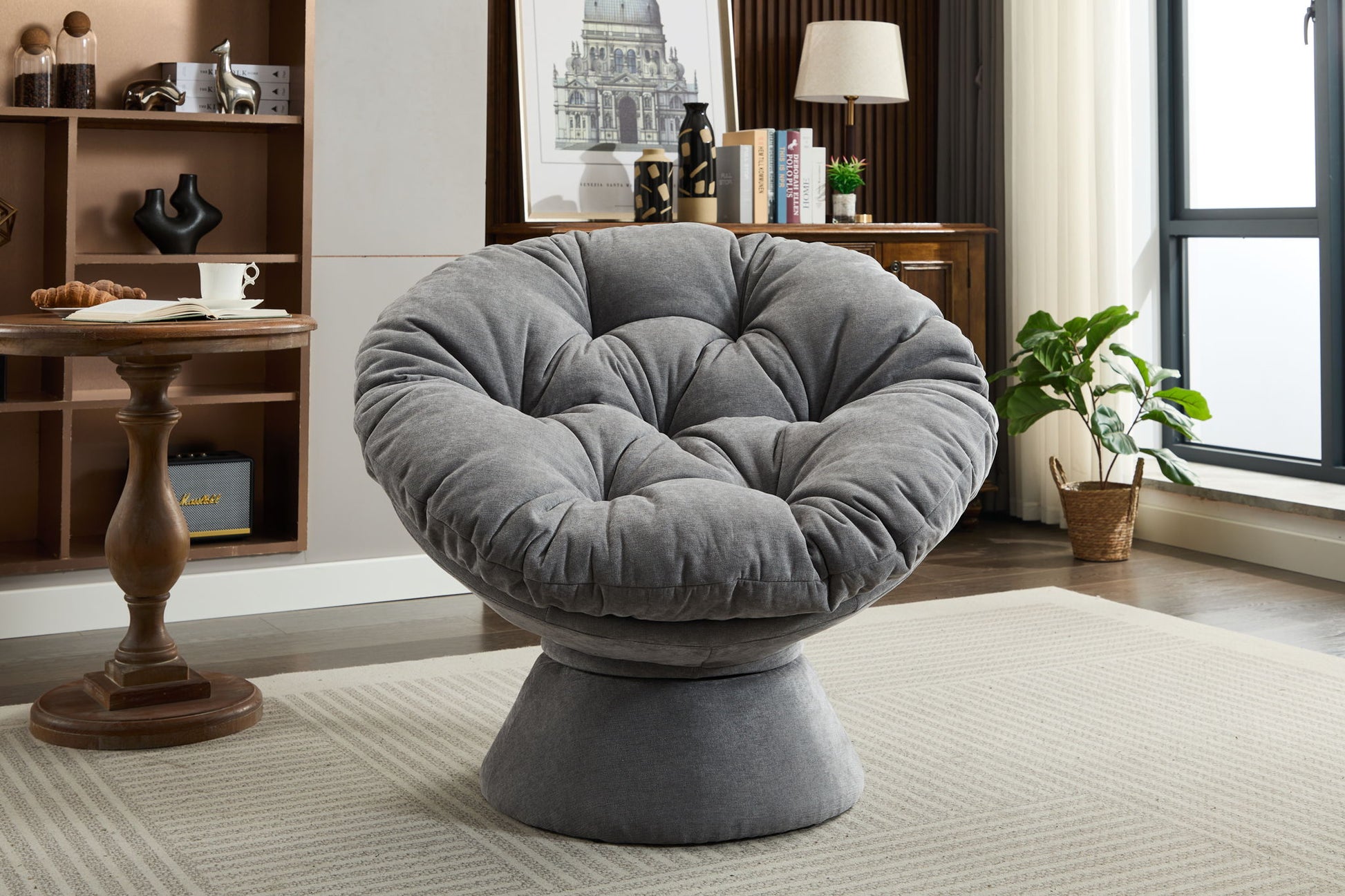 A modern living room with the Oversized Swivel Accent Chair, a plush round papasan-style seat on a light rug, paired with a wooden side table, bookshelf, potted plant, and natural light from a window.