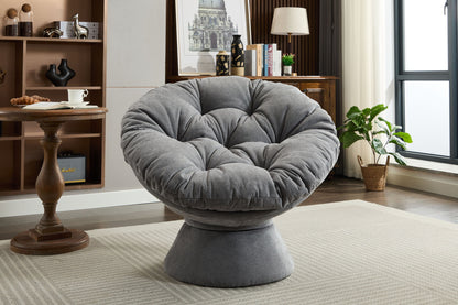 A modern living room with the Oversized Swivel Accent Chair, a plush round papasan-style seat on a light rug, paired with a wooden side table, bookshelf, potted plant, and natural light from a window.