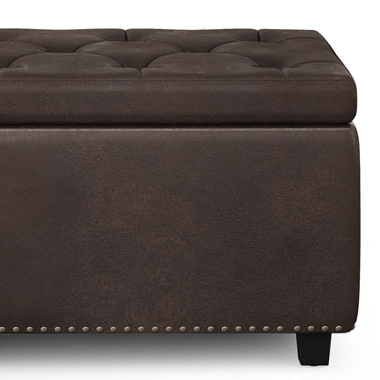Close-up of the Hamilton Upholstered Storage Ottoman featuring dark brown tufted leather, a cushioned top, decorative nailhead trim at the base, and short black legs.