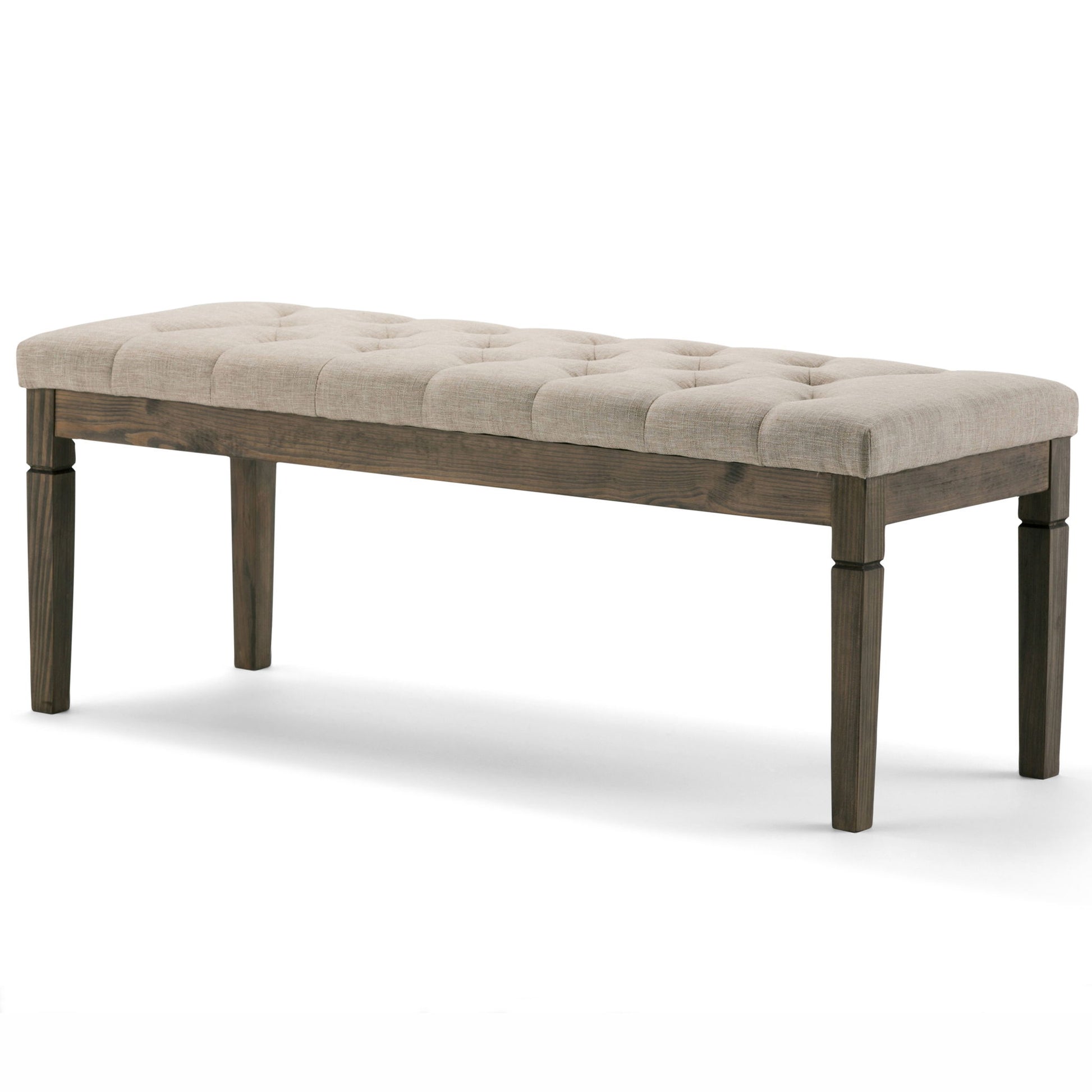 The Waverly Upholstered Tufted Ottoman Bench features a cushioned beige fabric seat with tufting and four dark wooden legs, shown against a plain white background.