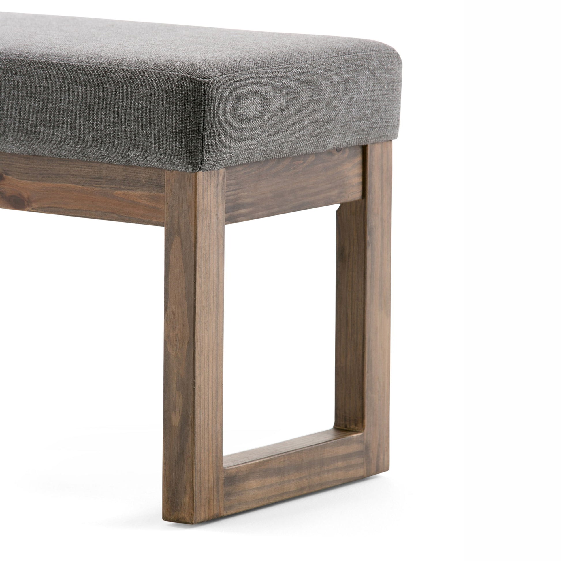 A close-up of the Milltown Upholstered Ottoman Bench, showcasing its gray upholstered seat and wooden legs with a rectangular open-frame design, set against a white background.