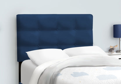 A modern bedroom featuring a large, dark blue upholstered transitional bed frame, white bedding, and a nightstand with a navy lamp and small moose figurine against a light wall.