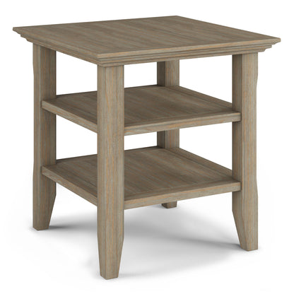 The Acadian - Handcrafted End Table features a square top, two lower shelves, and four straight legs. Its light, weathered wood finish creates a rustic farmhouse look.