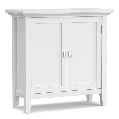 The Redmond Handcrafted Low Storage Cabinet features a white wooden finish, two paneled doors with silver handles, and four short legs, shown against a plain background.
