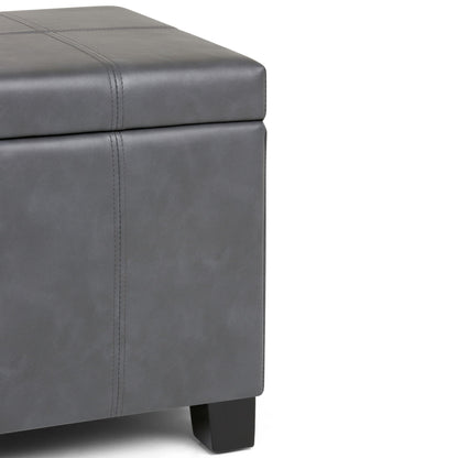A close-up of the Dover - Upholstered Storage Ottoman Bench, showcasing its modern gray leather or faux leather upholstery with visible stitching and dark wooden legs.