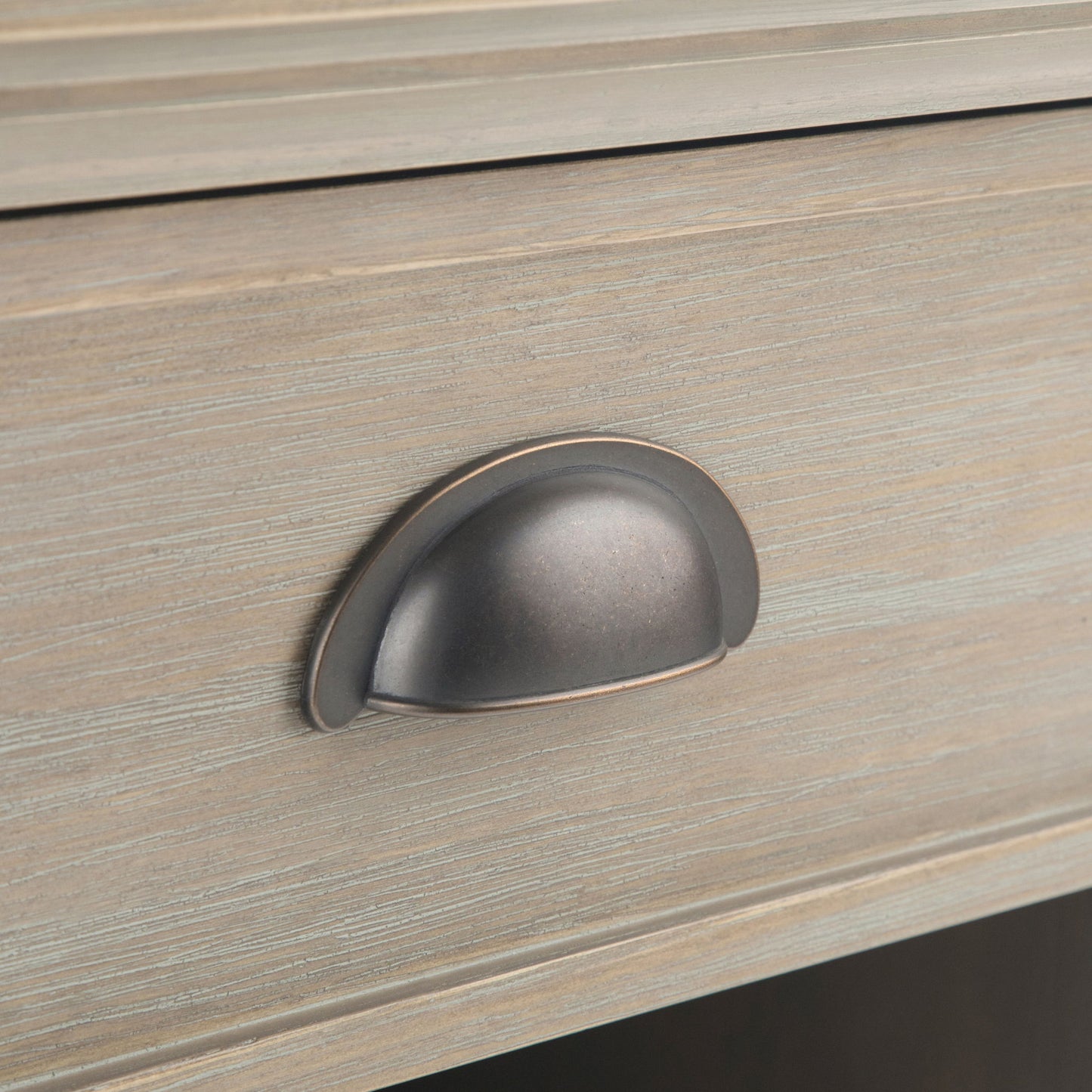 Close-up of the Acadian - Bedside Table, Handcrafted, showing a wooden drawer with a brushed metal cup pull. The light, weathered wood finish highlights horizontal grain and subtle texture.