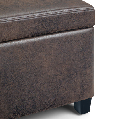 Close-up of the Avalon Storage Ottoman Bench in distressed brown faux leather, featuring visible stitching and short black wooden legs. The surface showcases a textured, weathered look.