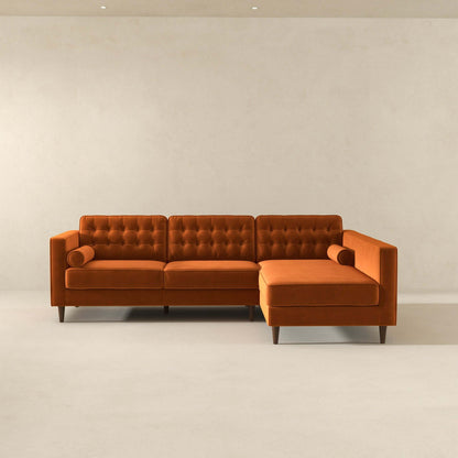 The Christian sectional sofa features mid-century modern design with orange tufted upholstery, two cylindrical pillows, and wooden legs, set in a minimal room with plain walls and a light floor.