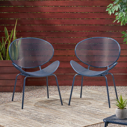 The Elba Contemporary Chair Set for Outdoor Relaxation features two modern, round metal chairs with mesh seats and backs, arranged on a rug over gravel by a wooden fence and potted plants in a garden setting.
