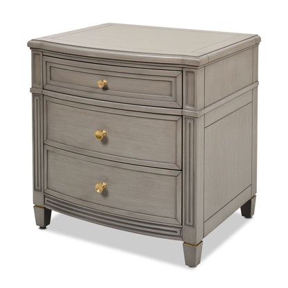 The Dauphin 3 Drawer Accent End Table is a gray wooden nightstand with three drawers, each featuring a round gold knob and slightly curved front panels, showcasing simple, classic detailing.