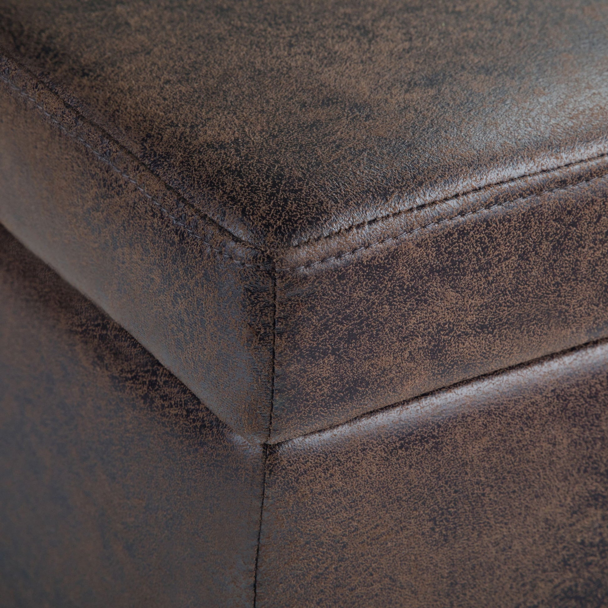 Close-up of the corner of the Avalon Storage Ottoman Bench in Distressed Brown, highlighting textured material, detailed stitching, and a slightly worn finish.