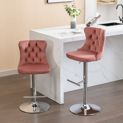 A set of two Swivel Velvet Barstools with tufted backs, chrome bases, and adjustable seat height (25-33") are placed by a white marble kitchen island featuring a vase, wine holder, and a sink.