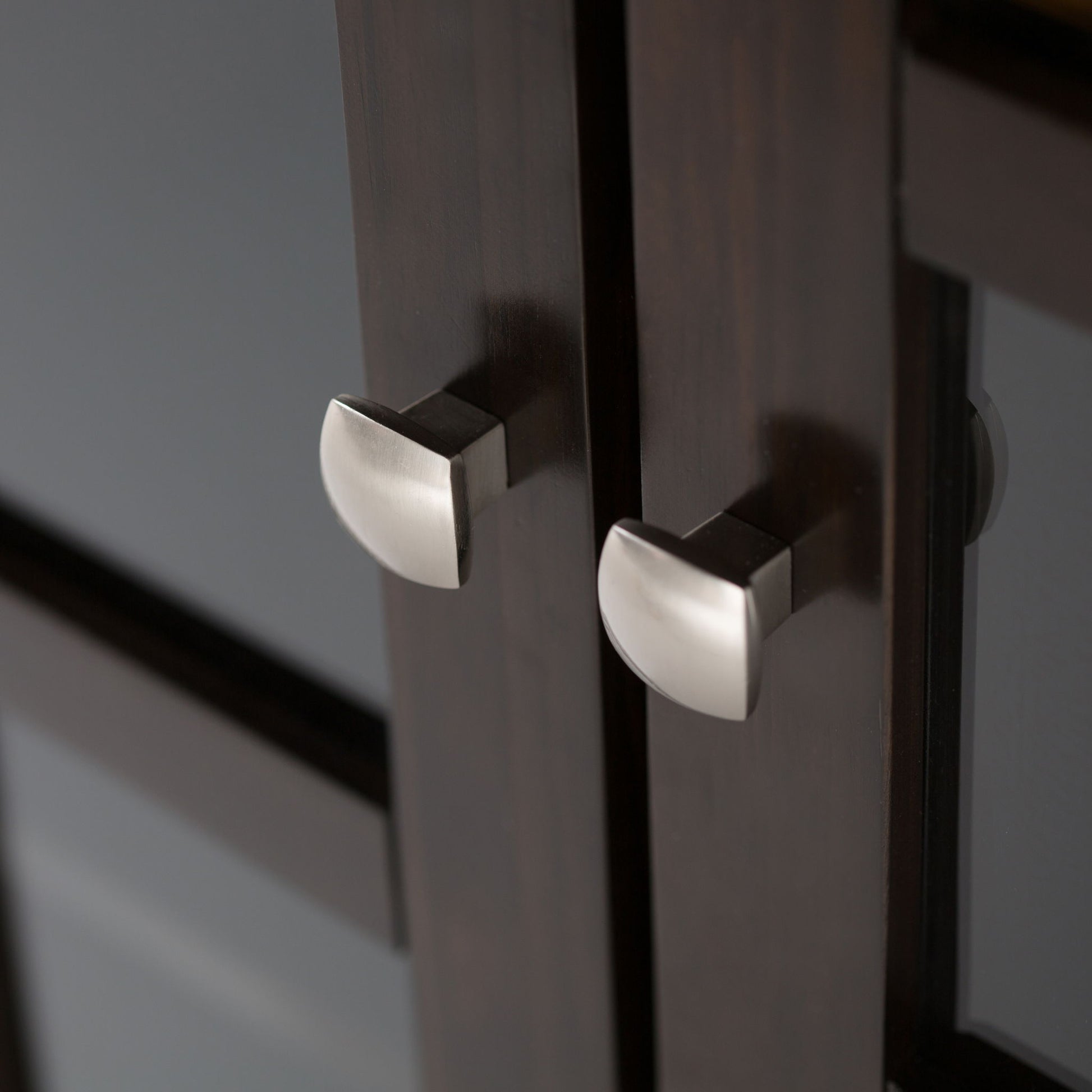 Close-up of two brushed metal handles on the Acadian - Medium Storage Cabinet, Handcrafted, with a soft reflection on the dark wooden doors.