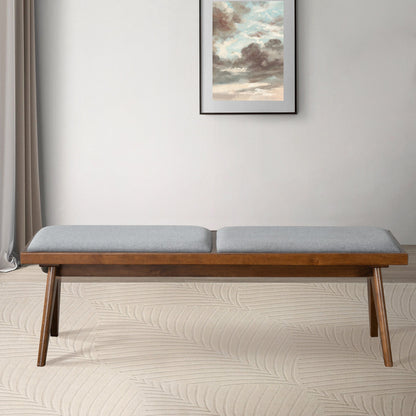 The Keira - Modern Aesthetics Bench with a light gray cushion sits on a beige patterned rug before a light wall accented by a framed cloud painting, with sheer curtains draped to the left.