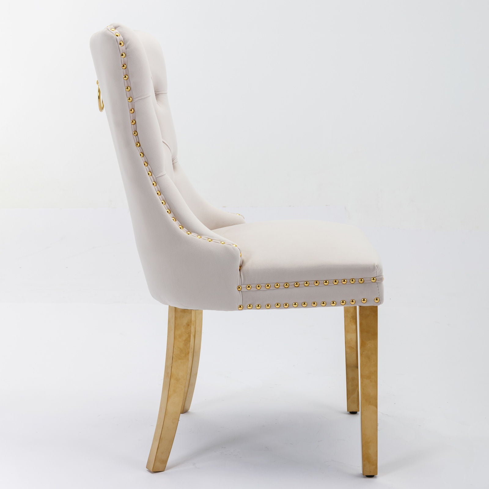 Side view of Nikki, a modern high-end dining chair set with luxe velvet upholstery, tufted backrest, nailhead trim, and solid wood legs accented with golden stainless steel plating, against a plain white background.