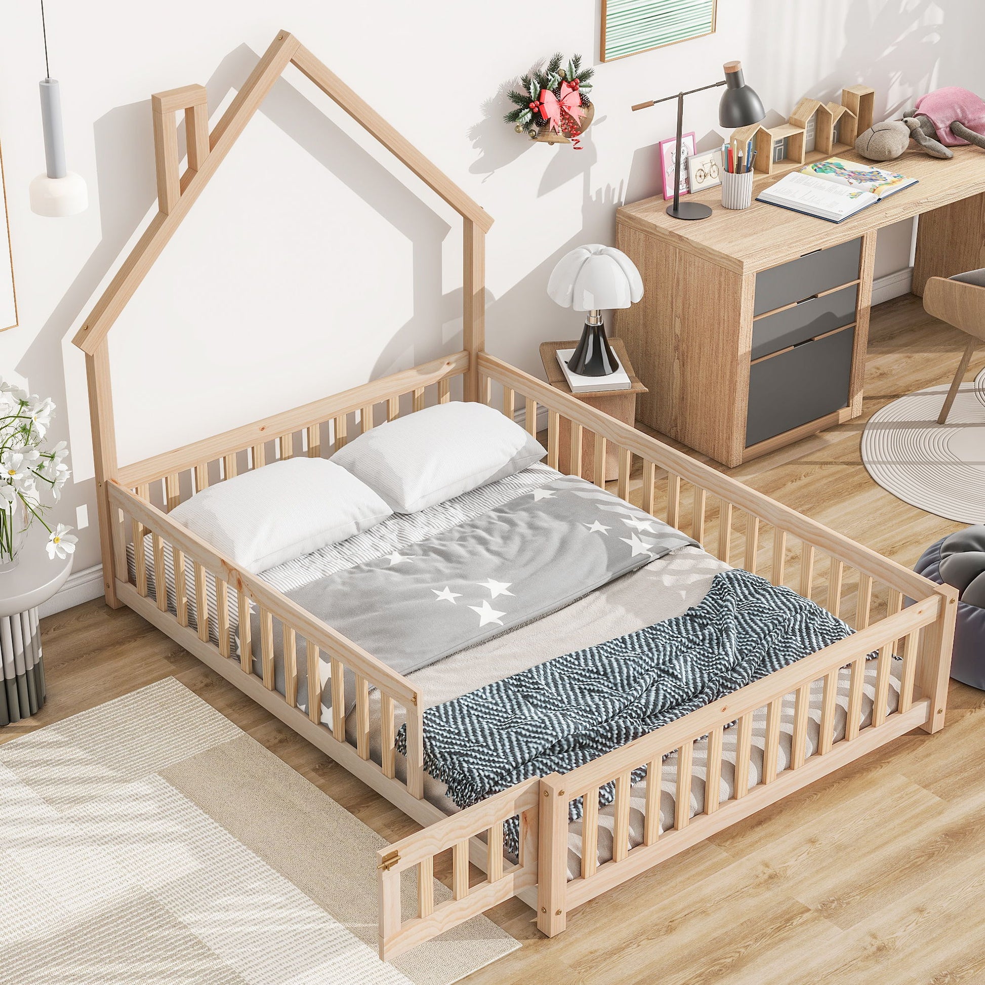 The House-Shaped Headboard Floor Bed With Fence, dressed with white pillows and a gray star-patterned blanket, stands in a bright bedroom featuring wooden furniture and decor.