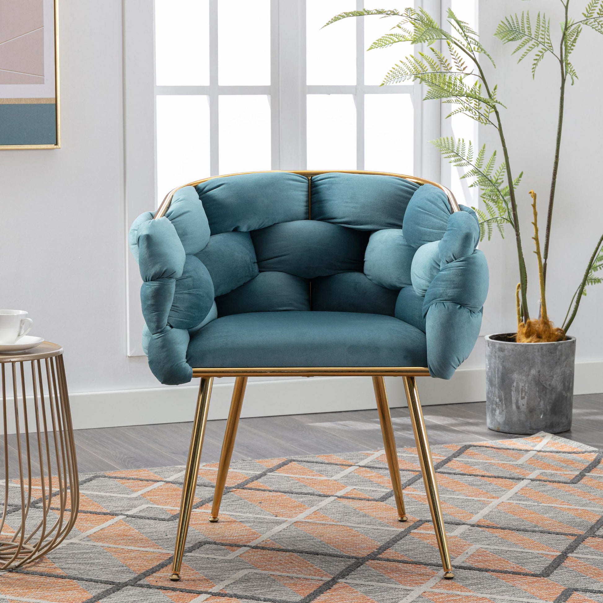 A Luxury Modern Simple Leisure Velvet Single Sofa Chair with tufted upholstery and gold legs sits on a geometric rug beside a plant and round side table in a bright room with large windows.
