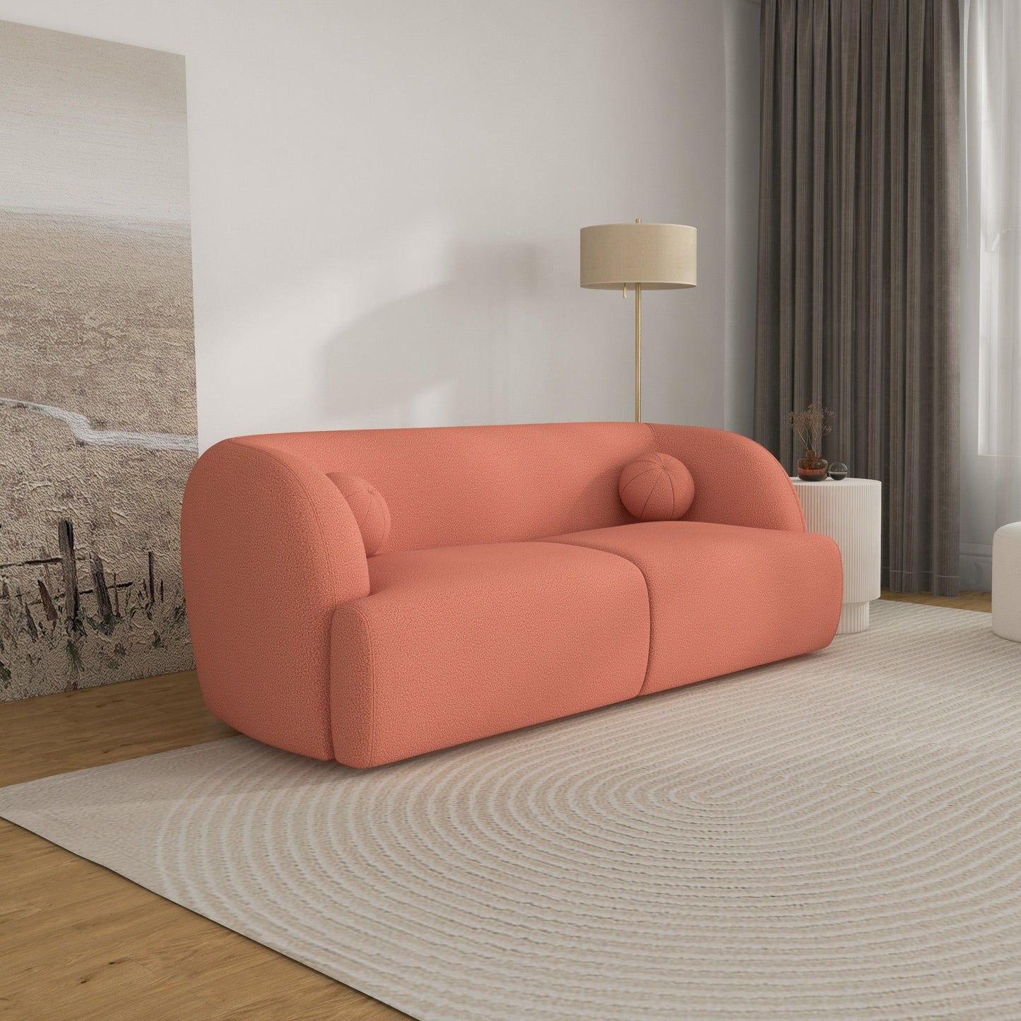 A modern living room featuring the Anna - French Boucle Sofa in coral, two round pillows, a beige floor lamp, a round white side table, a large circular-patterned rug, and landscape artwork leaning against the wall.