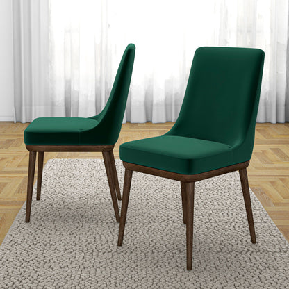 A set of two Kate Mid-Century Modern Dining Chairs with dark green cushions and wooden legs sit on a beige rug—one faces forward, the other in profile—in a room with wooden floors and white curtains.