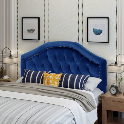 A cozy bedroom features a bed with the Kaarina Contemporary Tufted Fabric Headboard in blue, paired with striped and patterned pillows, neutral bedding, wooden nightstands with lamps, a clock, and framed art against patterned wallpaper.