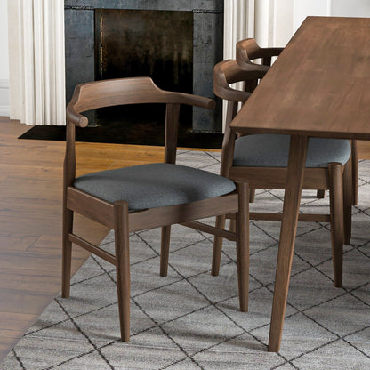 A set of Dakota Mid-Century Modern Velvet Dining Chairs with curved backs and dark gray cushions is placed by a matching dining table atop a patterned gray rug, with wood floors and a fireplace in the background.