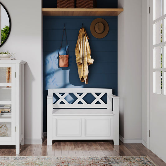 The Amherst - Small Transitional Entryway Storage Bench sits against a blue shiplap wall in a bright entryway. Above, hooks hold accessories, while two baskets are on a shelf nearby as sunlight casts soft shadows.
