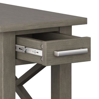 A close-up view of the Kitchener - Handcrafted Table shows its grayish wood finish and a partially open drawer with a metal handle and visible metal sliding mechanism.