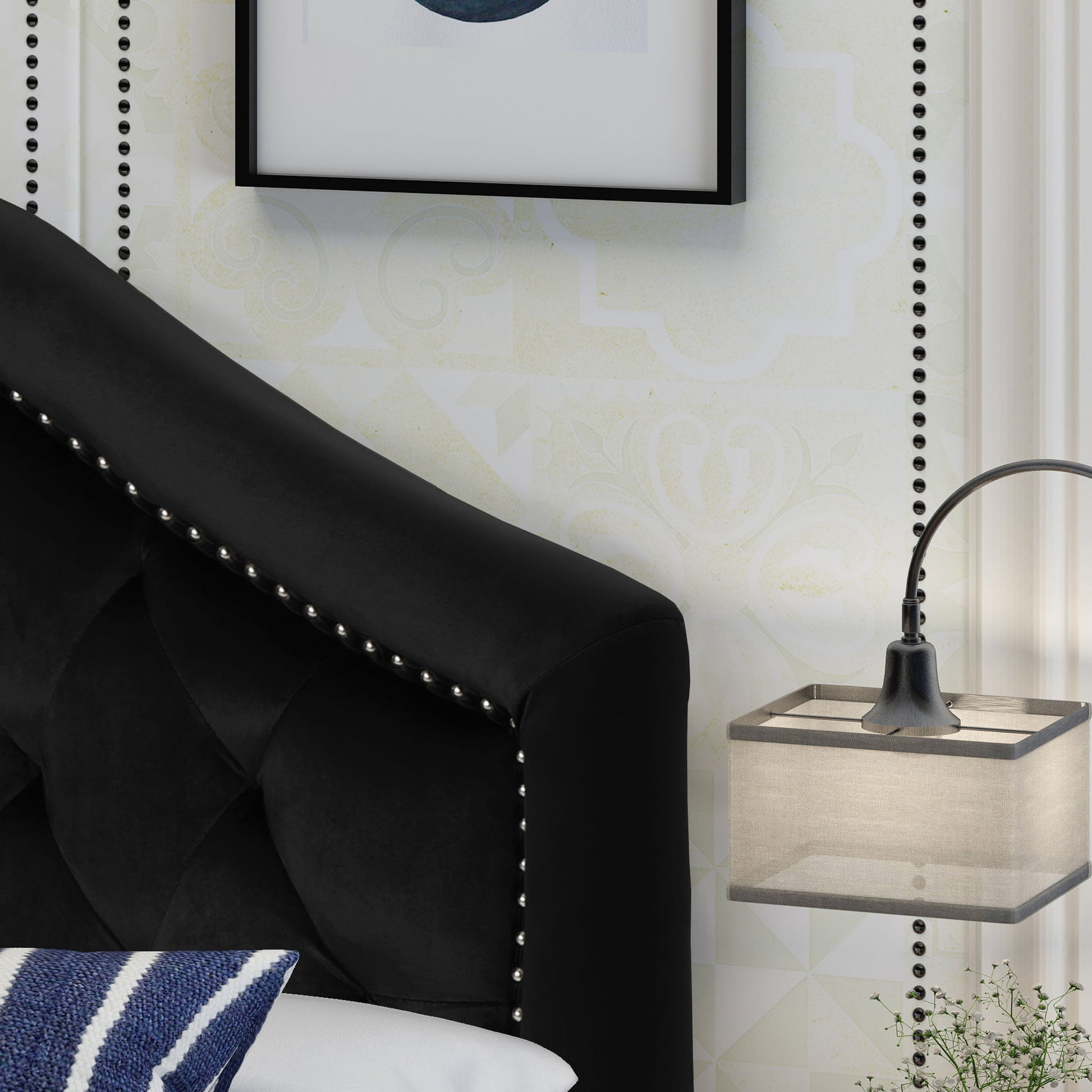 A close-up of the Kaarina - Contemporary Tufted Fabric Headboard in black with silver studs, beside a floating nightstand with a modern lamp, a white and blue pillow, subtle patterned wallpaper, and framed wall art above.