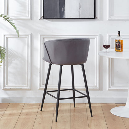 A set of Counter Height Bar Stool Metal Legs in modern gray velvet stands on a wooden floor beside a white round table with red wine and liquor, against a white paneled wall featuring a monochrome painting.