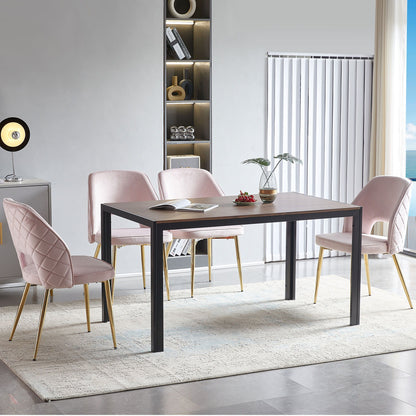 A modern dining room features a rectangular table, four Velvet Dining Chairs With Metal Legs And Hollow Back, a light rug, a decorative shelf in the background, plus books and a plant on the table and vertical blinds on the window.