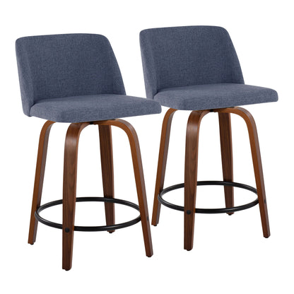 The Toriano set includes two mid-century modern counter stools with padded blue-gray fabric seats and backs, curved wooden legs, black metal round footrests, and a fixed height swivel design. Shown against a white background.
