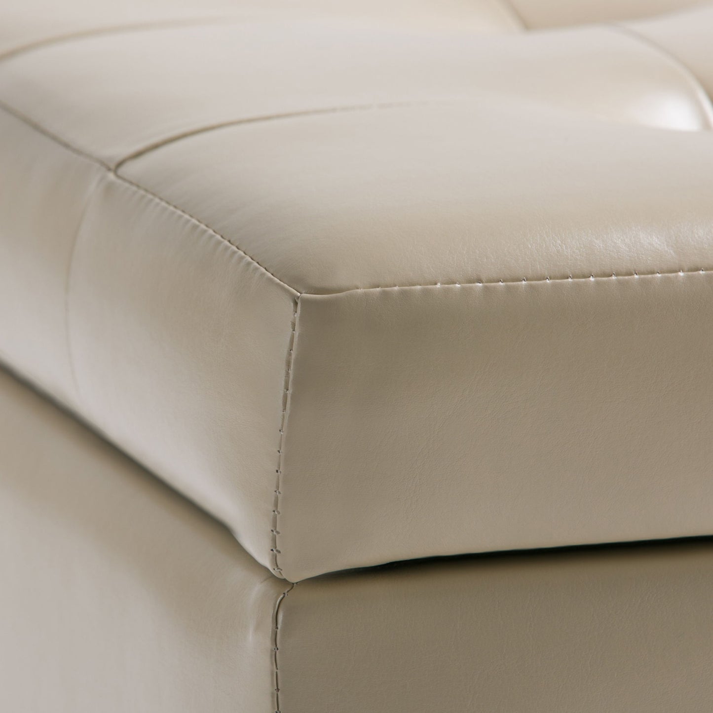Close-up of the Cosmopolitan - Upholstered Storage Ottoman in beige leather, featuring visible stitching, tufted details, and a matching base.