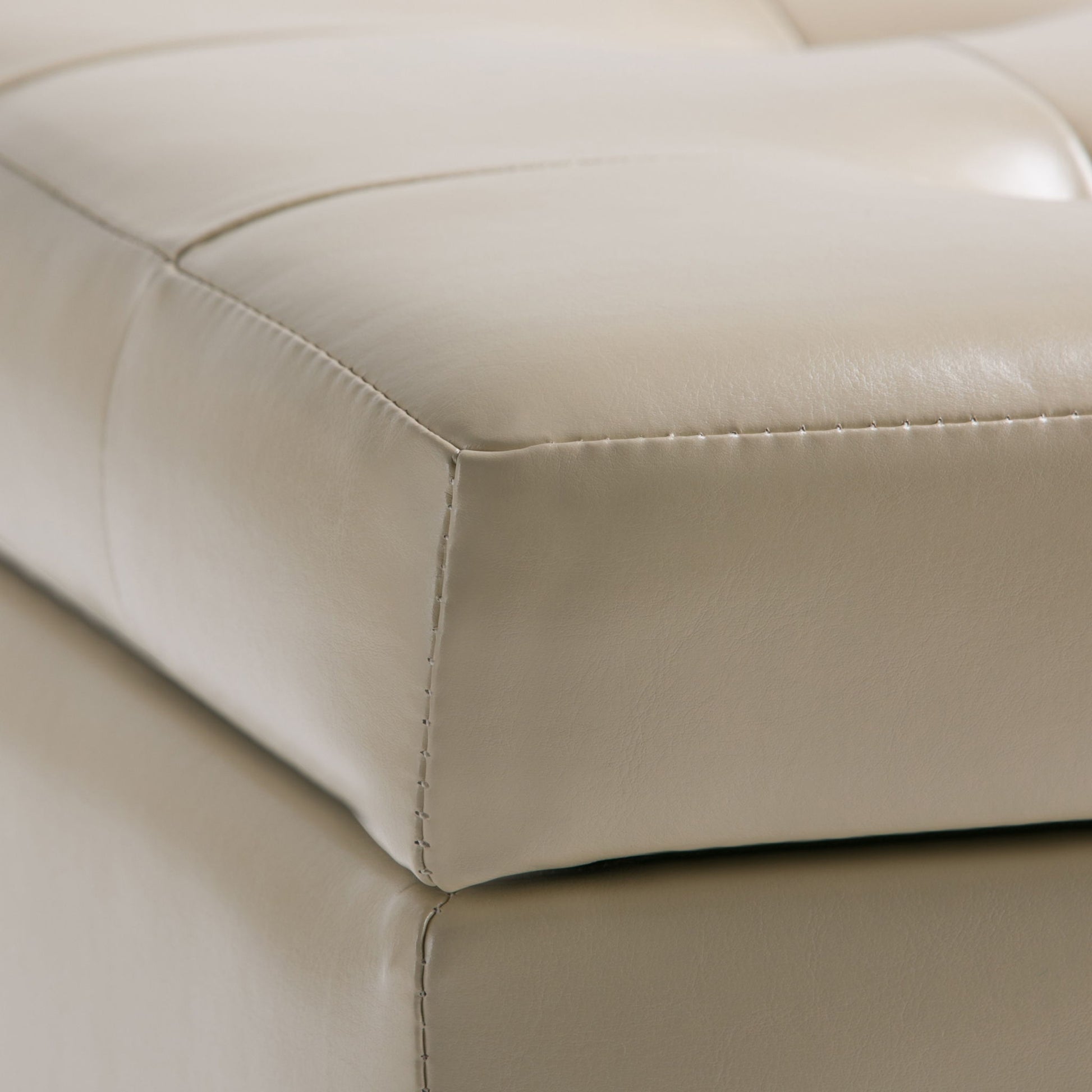 Close-up of the Cosmopolitan - Upholstered Storage Ottoman in beige leather, featuring visible stitching, tufted details, and a matching base.