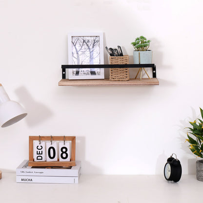 A minimalist desk setup features a calendar showing December 8, lamp, black clock, and plant. Above, natural wood floating wall shelves hold a framed photo, plant, and two woven containers with pens.