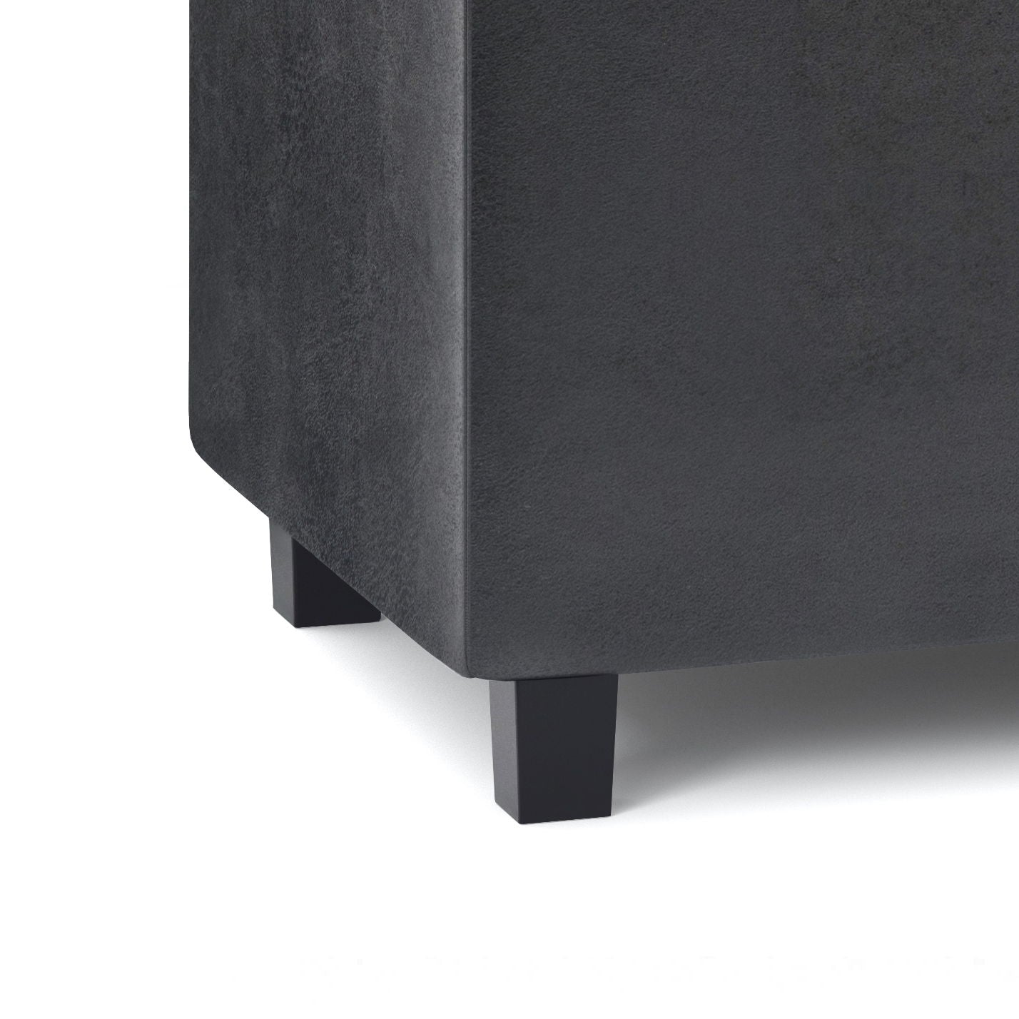 Close-up of the bottom corner of the Cosmopolitan - Upholstered Storage Ottoman in dark gray, highlighting two short black rectangular legs and the fabric’s texture.