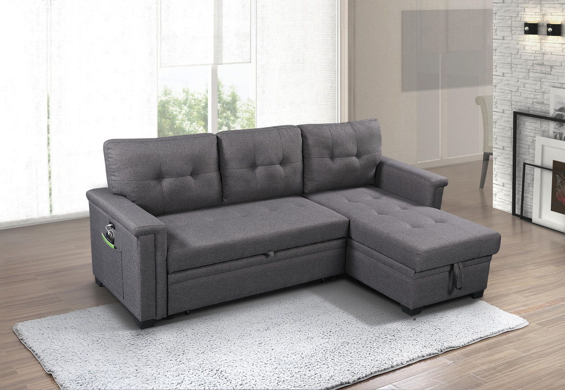 The Ashlyn Reversible Sleeper Sectional Sofa with Storage Chaise, USB charging ports, and pocket is featured on a light gray rug in a bright living room with wood flooring and contemporary decor.