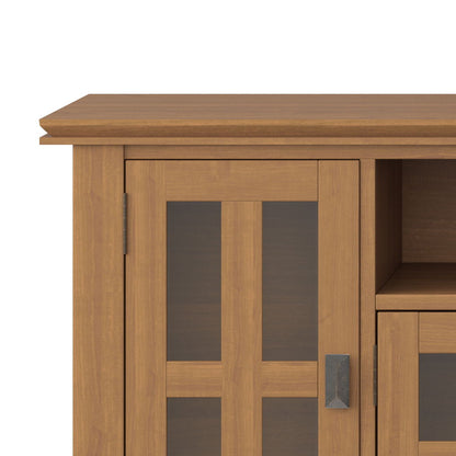 A close-up of the Artisan TV Media Stand features a light brown wooden finish, glass-paneled door, metal handle, and visible interior shelving.