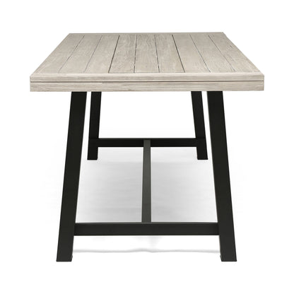 The Equilibrium Outdoor Dining Table features a light wooden slat top and black metal legs, shown from the short end against a white background.