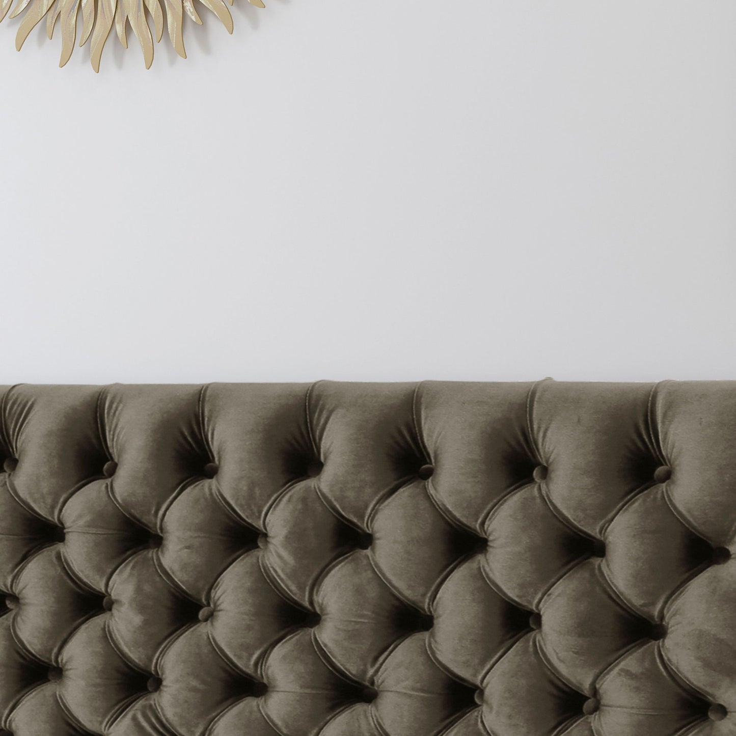 The Annecy - Contemporary Upholstered Headboard in dark gray stands against a white wall, with a decorative gold sunburst mirror partially visible in the upper left corner.